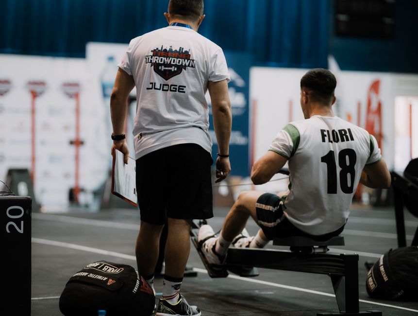 A judge oversees a rowing competitor in a dynamic sports event indoors.